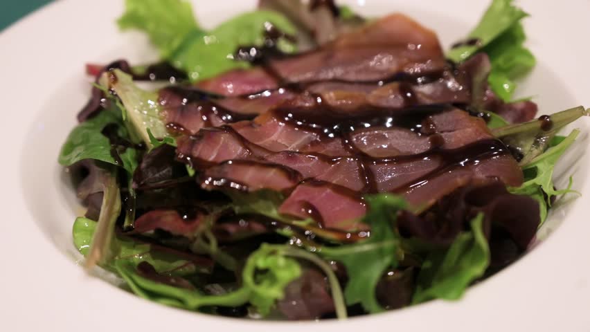A dish of sliced smoked tuna and salad, topped with sweetened vinegar ready to be eaten.
