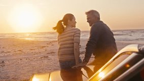 Rear view of retired senior couple on vacation sitting on hood of classic convertible sports car at beach watching morning sunrise on road trip - shot in slow motion - Powered by Shutterstock - Get 15% off with code: PIKWIZARD15