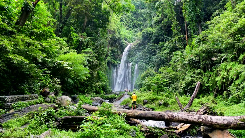 Man with yellow rain jacket watching the waterfall in Sendang Gile Waterfall.