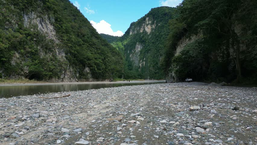 Low flight over riverbank at Muchas Aguas with people relaxing in background, Dominican Republic. Aerial forward 