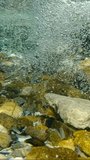Vertical footage, Movement downstream of a stream with air bubbles, Slow motion. Natural underwater background of air bubbles in a stormy stream of a mountain river.