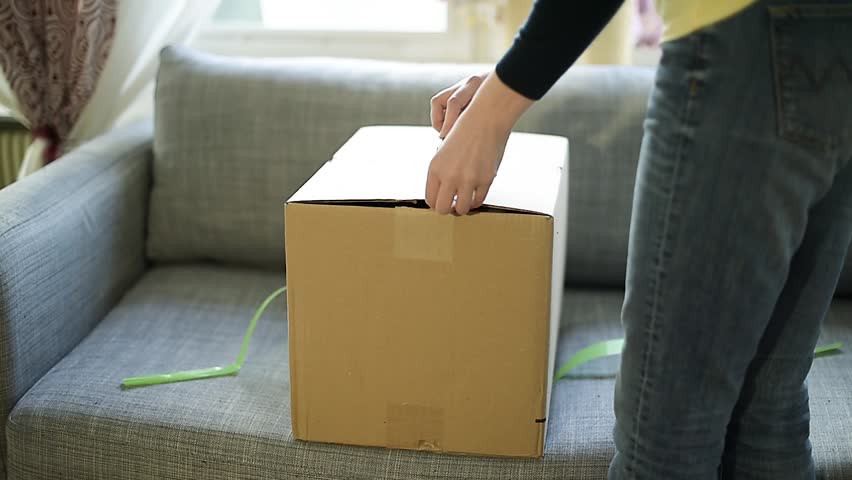 Young woman unboxing unpacking box received by parcel post in the living room couch | Shutterstock HD Video #34509772