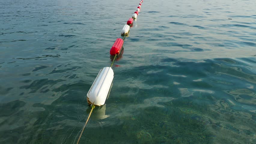 Buoy swim area marker. Visible channel marker coated with durable white and marine red enamel for increased durability. Assembling barrier and swim areas. Buoys on the water, Adriatic Sea, Montenegro. Royalty-Free Stock Footage #3451010793