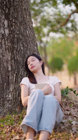 Asian woman peacefully journaling and taking a nap at the public park. Finding tranquility in nature
