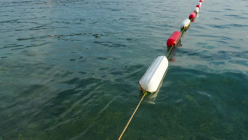 Buoy swim area marker. Visible channel marker coated with durable white and marine red enamel for increased durability. Assembling barrier and swim areas. Buoys on the water, Adriatic Sea, Montenegro. Royalty-Free Stock Footage #3451019295