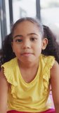 Vertical video of portrait of happy biracial girl wearing yellow dress looking at camera. spending time at home.