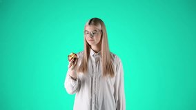 Caucasian woman with glasses eating apple, taking a bite, turquoise background - Powered by Shutterstock - Get 15% off with code: PIKWIZARD15