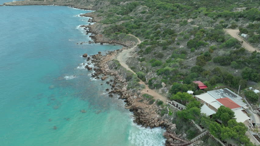 An aerial shot of Konnos Beach in Ayia Napa, Cyprus, highlights a secluded cove with golden sands, clear blue waters, and surrounding greenery, a perfect spot for relaxation and swimming