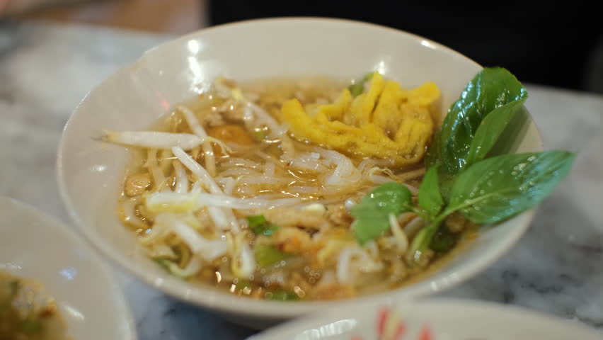 Close-up of female eating tasty spicy Asian noodle soup indoors, slow motion. Traditional Thai food concept