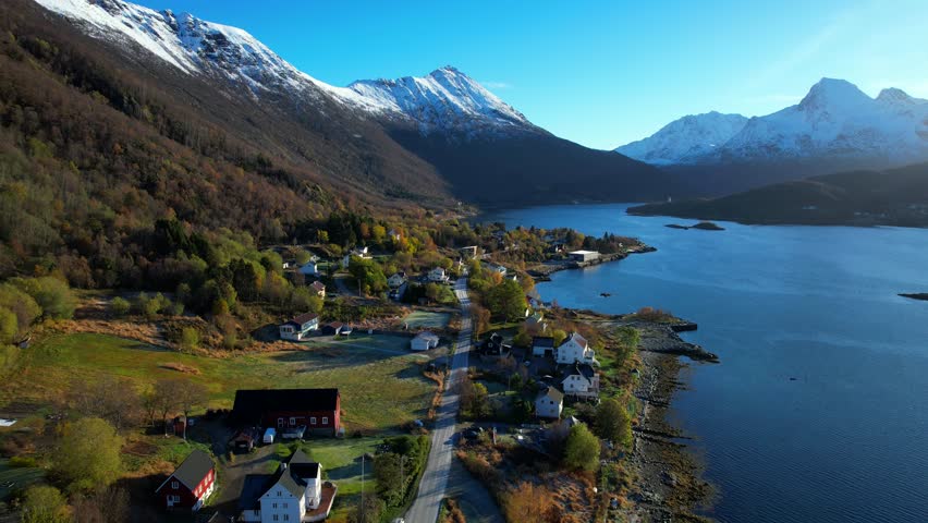 Aerial forwarding shot inside a Norwegian Fjord with a small traditional settlement and snow capped mountains Royalty-Free Stock Footage #3451300501