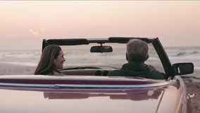 Retired senior couple on vacation driving classic convertible sports car onto beach to watch morning sunrise on road trip - shot in slow motion - Powered by Shutterstock - Get 15% off with code: PIKWIZARD15
