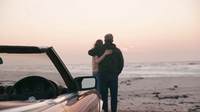 Camera pushes in on rear view of retired senior couple on vacation standing by classic convertible sports car at beach watching morning sunrise on road trip - shot in slow motion - Powered by Shutterstock - Get 15% off with code: PIKWIZARD15