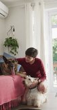 Vertical video of happy caucasian woman petting her dogs at home. spending time together at home.