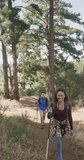 Vertical video of biracial couple hiking with trekking poles in forest, slow motion. Spending quality time, lifestyle, nature, hiking and camping concept.