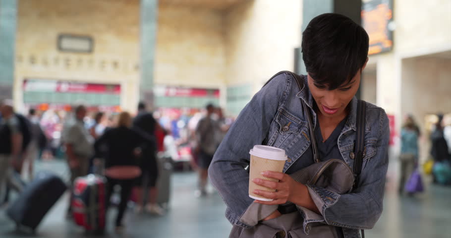 Gorgeous African woman takes her smartphone out of her purse to see a recent text message. Young African-American female at train station lobby with coffee checks her phone. 4k