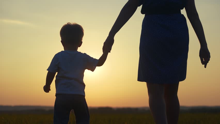 mom and son in the park. mom holding her son hand walking in the park silhouette at sunset in nature. happy family kid dream lifestyle concept. mom and son family walking in nature