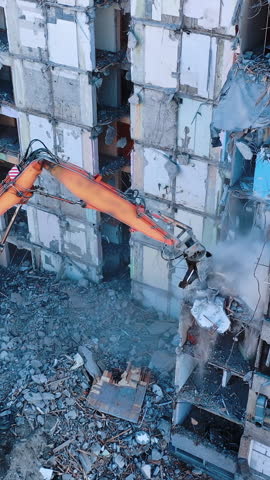 Dismantling of a high bulding. Excavator demolishing ruins for new construction project. Flying above a destruction. Vertical video.