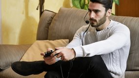 Young handsome man playing video game and talking with online players through headset, while sitting on couch at home at night