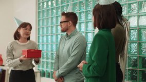 Happy business team of office employees wearing festive caps in modern office giving gift to handsome male coworker on birthday. Cheerful man surprised to open box with gift to applause of coworkers. - Powered by Shutterstock - Get 15% off with code: PIKWIZARD15
