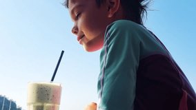 The boy drinkink sweet milk coctail in restaurant near the sea. 4k video footage in slow motion