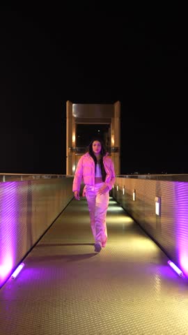 Low angle view of a happy trap dancer in pink clothes dancing alone outdoors at night