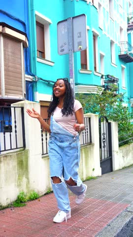 African woman singing to the camera and dancing in the street next to a blue house