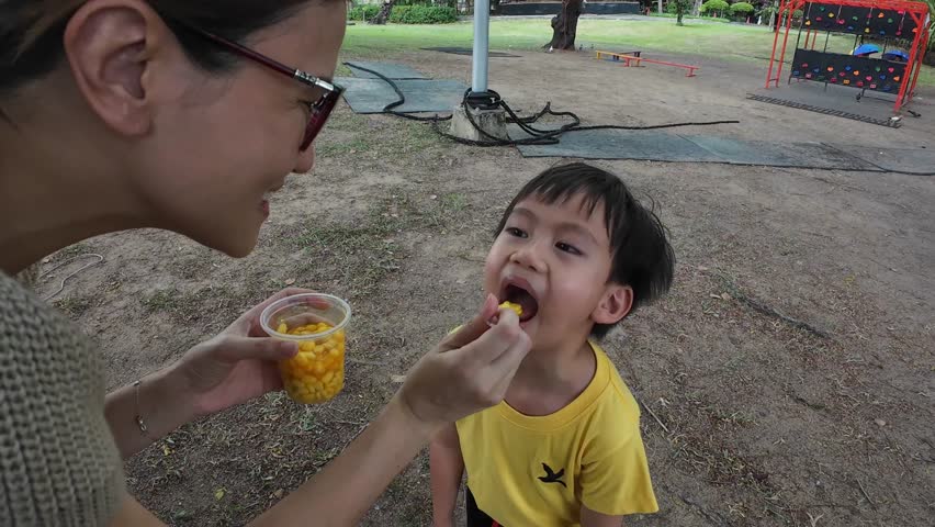 A mother is feeding her son delicious snacks.