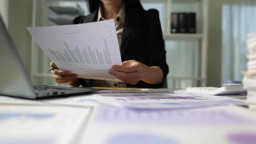 Serious Asian businesswoman is busy with paperwork on a messy desk. Woman are stressed due to excessive workload and are forced to overworked. Royalty-Free Stock Footage #3451649539