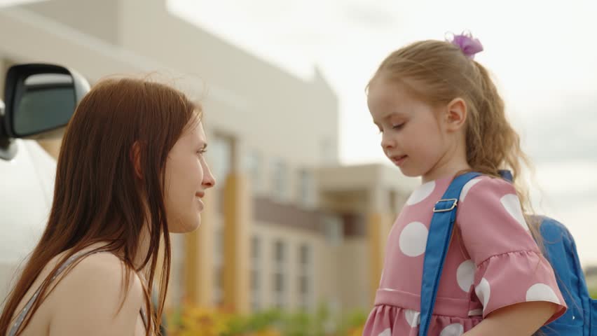 Happy mother see off cute little daughter to primary school hugging with love outdoor closeup. Smiling young woman embracing girl kid child pupil going elementary education lesson at campus schoolyard Royalty-Free Stock Footage #3451763733