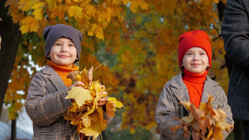 Daughter with son enjoy throwing autumn leaves up with parents. Preschooler children hold autumn leaves standing near parents. Happy boy and girl spend time together with parents among autumn leaves