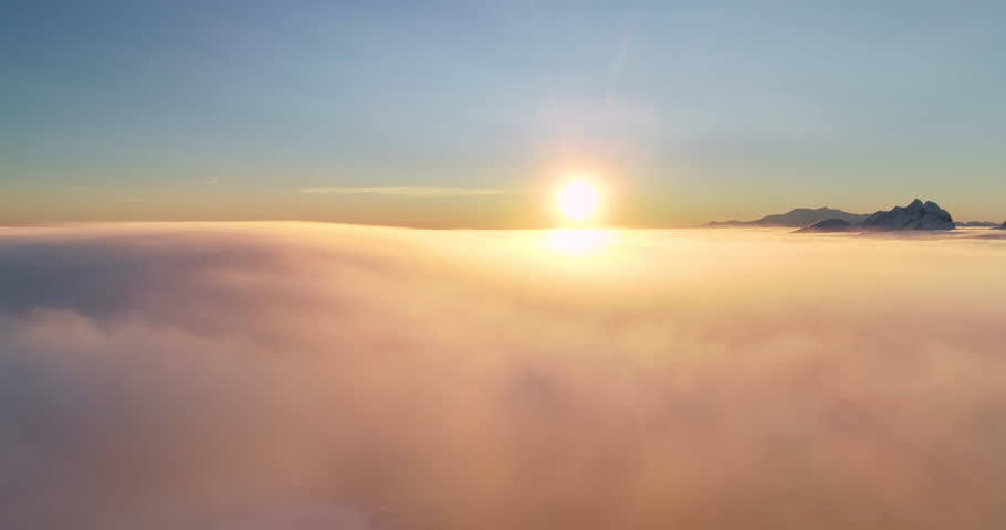 Mountain peak over sunset orange clouds sky. Tranquil scene morning sunrise fog sea overview. Sun shine over horizon, warm light texture. Nature background perfect landscape. Aerial panoramic flight