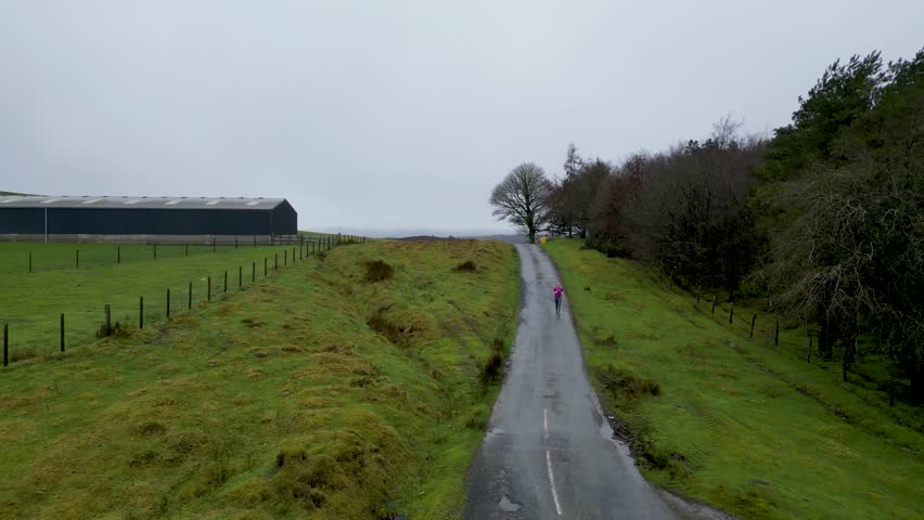 Aerial view of a young caucasian woman running down a country road in winter British weather. Model released.