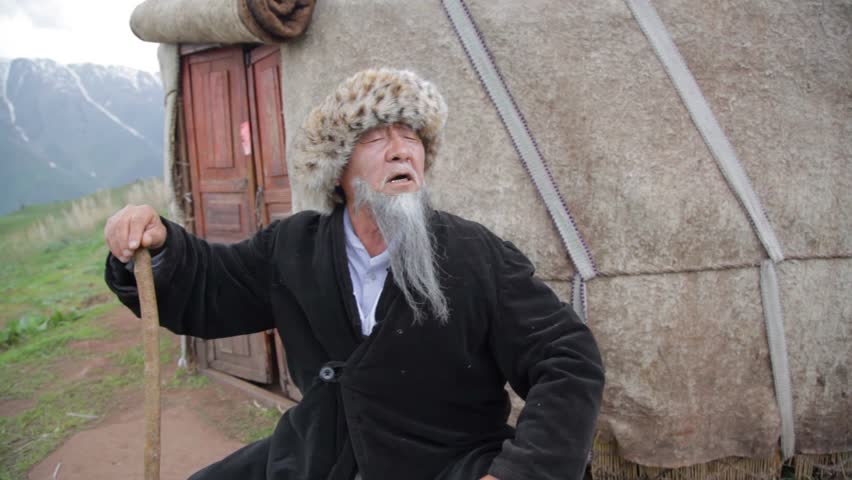 A mysterious old man stands on a rock and stares intently. A man in Kyrgyz national clothes