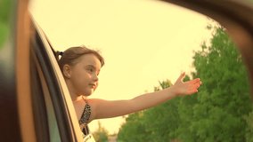 Little girl, child traveling by car. Child trip, Video in rear view mirror. Child smiles, enjoys family vacation, car trip. Happy child is driving in car, looking out window with an outstretched hand.