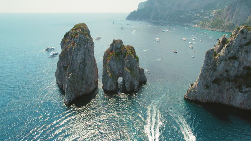 Majestic sea stacks rise from the blue waters of Capri, Italy. Vessels float around natural rock formations on the Tyrrhenian Sea. Royalty-Free Stock Footage #3451910051