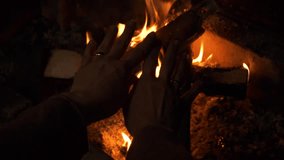 Woman warming her hands by the cozy fireplace with burning firewood, close-up view.