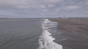 Low altitude wide-angle aerial drone footage of ocean waves breaking on a sandy beach on a cloudy day at Westport, Washington.