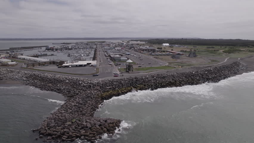 Ungraded aerial drone footage surveys the coastal town of Westport, Washington, with views of the marina and protective sea barriers.
