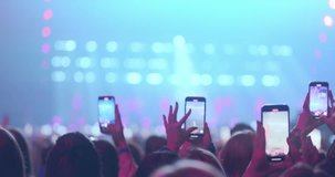 People raising smartphones record live performance, capturing vibrant stage lights, concert energy. Silhouetted female hands filming glow of stage in pink spotlights, on blur music show background