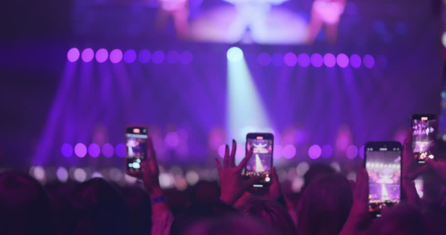 People raising smartphones record live performance, capturing vibrant stage lights, concert energy. Silhouetted female hands filming glow of stage in pink spotlights, on blur music show background