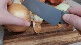woman's hands peeling onion with a knife over a wooden board with shallow focus.