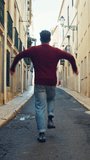 Vertical Screen: Cheerful Young Adult Man in Casual Clothes Actively Dancing while Walking on the Street of an Old Town in a City. Scene Shot in an Urban Environment on an Quiet Small Town Street