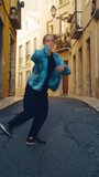 Vertical Screen: Beautiful Young Adult Woman in Stylish Clothes Actively Dancing Hip Hop on the Street of an Old Town in a City. Scene Shot in an Urban Environment on an Quiet Small Town Street
