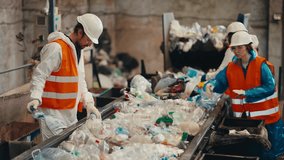 Shot from the side three workers in white uniforms in orange vests sort garbage near a conveyor belt transferring plastic bottles by color into the appropriate boxes at a waste recycling plant - Powered by Shutterstock - Get 15% off with code: PIKWIZARD15