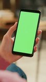 Vertical Screen: Feminine Hand Scrolling Feed on Smartphone with Green Screen Mock Up Display. Female Resting at Home and Checking Social Media on Mobile Device. Close Up Over the Shoulder Footage.