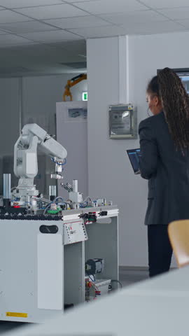At the Factory: Black Developer Uses Laptop for Programming Robotic Arm while Standing at Table In Front of Robot. New Era in Automatic Manufacturing Industry Concept. Vertical Screen Royalty-Free Stock Footage #3452167653