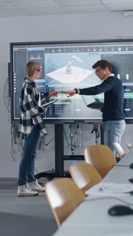 Two Male and Female Students Standing Near Big Screen and Discussing Program for Motion of Robotic Arm. People holding Computers. Startup and Innovative Technologies Concept. Vertical Video Royalty-Free Stock Footage #3452168339