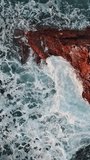 Aerial top view of waves and rocks in the sea. Vertical video