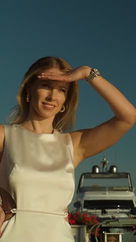Stylish and beautiful blonde woman in fashionable attire smiles on a sunny summer day against the backdrop of yachts