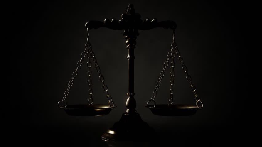 A single light glinting across the surface of a  gold ornate justice scale backlight a dim black background